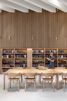 a man standing in front of a book shelf filled with books next to wooden tables and chairs