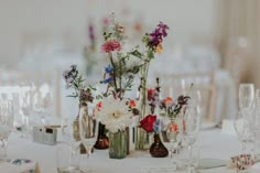 an arrangement of flowers in vases and wine glasses on a table set for a wedding reception