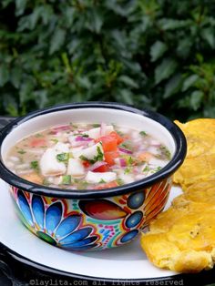 a bowl of soup with tortilla chips on a plate next to some bushes