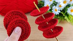 a hand is holding two red knitted hearts on a wooden table next to yarn and flowers