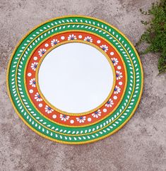 a round mirror sitting on top of a cement floor next to green and red flowers