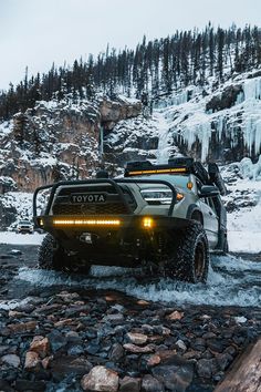 a truck is driving through the water in front of a mountain with ice on it