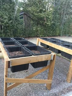 several black plastic containers sitting on top of a wooden table in front of some trees