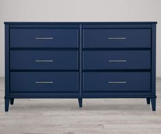 a dark blue dresser with gold handles and drawers on the bottom, against a white wall