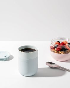 a bowl of cereal and a cup of coffee on a white table with a spoon