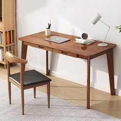 a wooden desk with a laptop on it and a chair next to it in front of a white wall