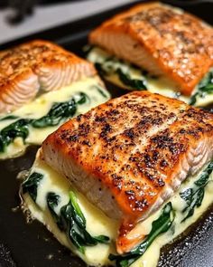 four pieces of salmon with spinach and cheese on a black plate next to an oven