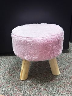 a pink stool with wooden legs on carpeted floor