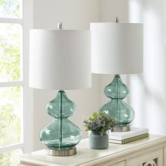 two green glass lamps sitting on top of a white table next to a lamp shade