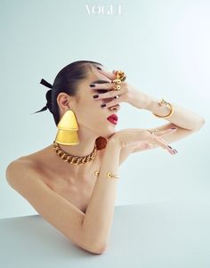 a woman with her hands on her face and wearing gold jewelry, posing against a white background