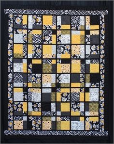 a black and yellow quilt with white flowers on the border is hanging in front of a wall