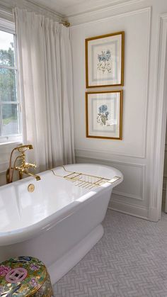 a white bath tub sitting in a bathroom next to two framed pictures on the wall