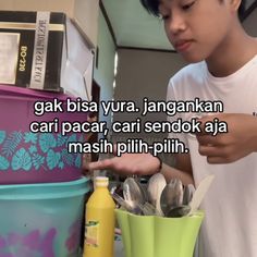 a young man standing next to a stack of plastic containers with spoons in them