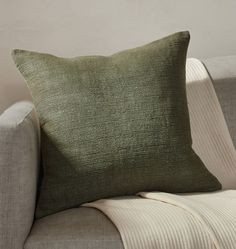 a green pillow sitting on top of a couch next to a white chair and wall