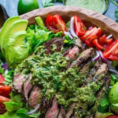 a steak salad with avocado and tomatoes on the side in a wooden bowl