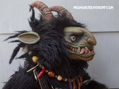 a stuffed animal with horns and teeth on it's head is sitting next to a wall