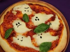 a pizza topped with cheese and ghost faces on top of a wooden plate sitting on a purple surface