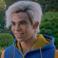 a young man with white hair wearing a blue and yellow jacket smiles at the camera