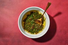 a white bowl filled with green food on top of a red tablecloth next to a wooden spoon