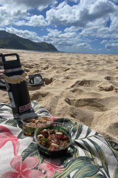 a bowl of food sitting on top of a beach next to a drink and water bottle