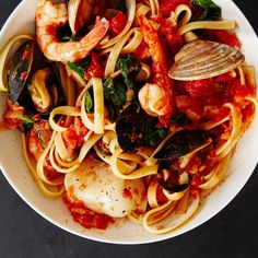 a bowl of pasta with shrimp, mussels and sauce on a black surface