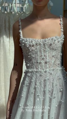 a woman in a white dress standing next to a window