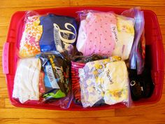 a red plastic container filled with lots of baby clothes and diapers on top of a wooden floor