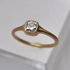 a gold ring with a white diamond in the center on a white box, close up