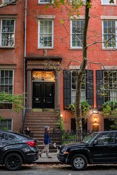 two cars parked in front of a red brick building with stairs leading up to the door