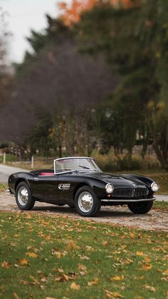 an old black sports car parked on the side of a road in front of trees