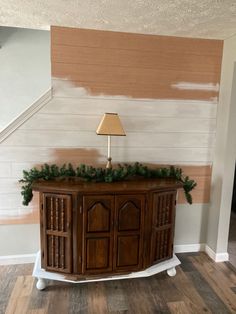 a wooden cabinet with christmas garland on top and a lamp in the corner next to it