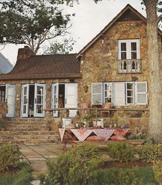 an old stone house with white shutters on the front and side windows, sitting next to a tree