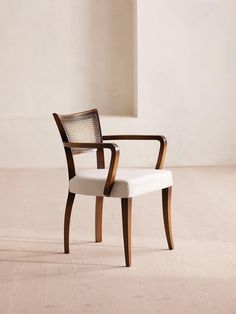 a wooden chair with white upholstered fabric on the seat and back, in an empty room