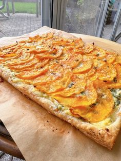 a pizza sitting on top of a wooden cutting board next to a glass door with an open window