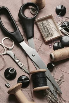 scissors, thread, and other crafting supplies on a pink table cloth with buttons