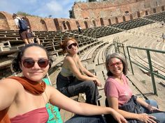 three women are sitting on the bleachers at an ancient amphite in italy