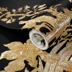 a black and gold wallpaper with golden leaves on it's side, next to a roll of metallic foil