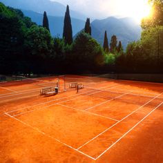 two tennis courts with benches and trees in the background