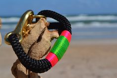 a close up of a bracelet on a beach with the ocean and sky in the background