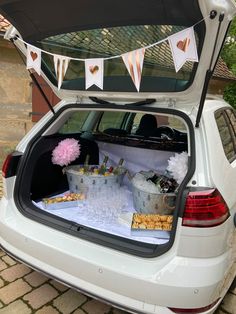 an open hatchback car trunk filled with food and drinks on a brick driveway next to a house