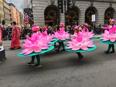 some people are walking down the street with large pink flowers on their heads and legs