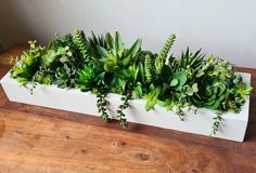 a white planter filled with green plants on top of a wooden table