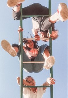 two people standing on top of a green ladder with their feet up in the air