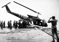 a group of people standing around a helicopter on top of an aircraft carrier with it's doors open