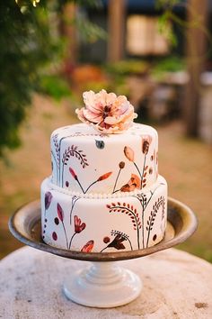 a three tiered cake decorated with flowers on a metal platter in the garden