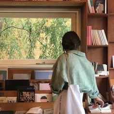 a woman standing in front of a bookshelf holding a bag and looking out the window