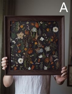 a woman holding up a framed painting with flowers on it