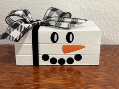 a wooden box with a black and white snowman face painted on it, tied with a bow