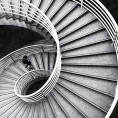 black and white photograph of spiral staircase with person sitting on the railing looking down at them