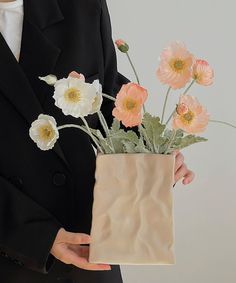 a woman holding a vase with flowers in it and wearing a black blazer over a white shirt